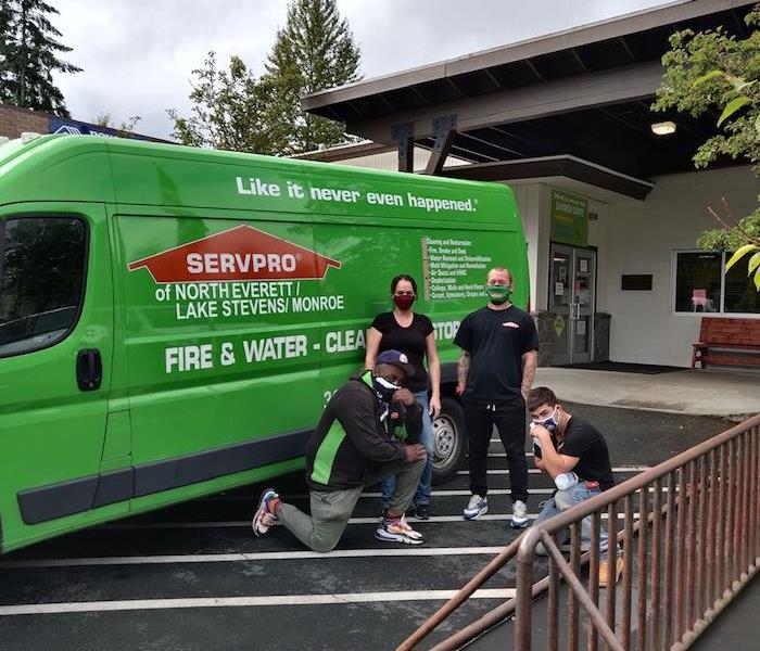 4 employees standing in a parking lot in front of a SERVPRO van