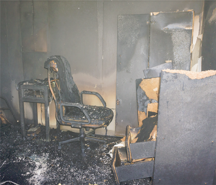 a fire damaged office with debris all over the floor and a soot covered chair and desk